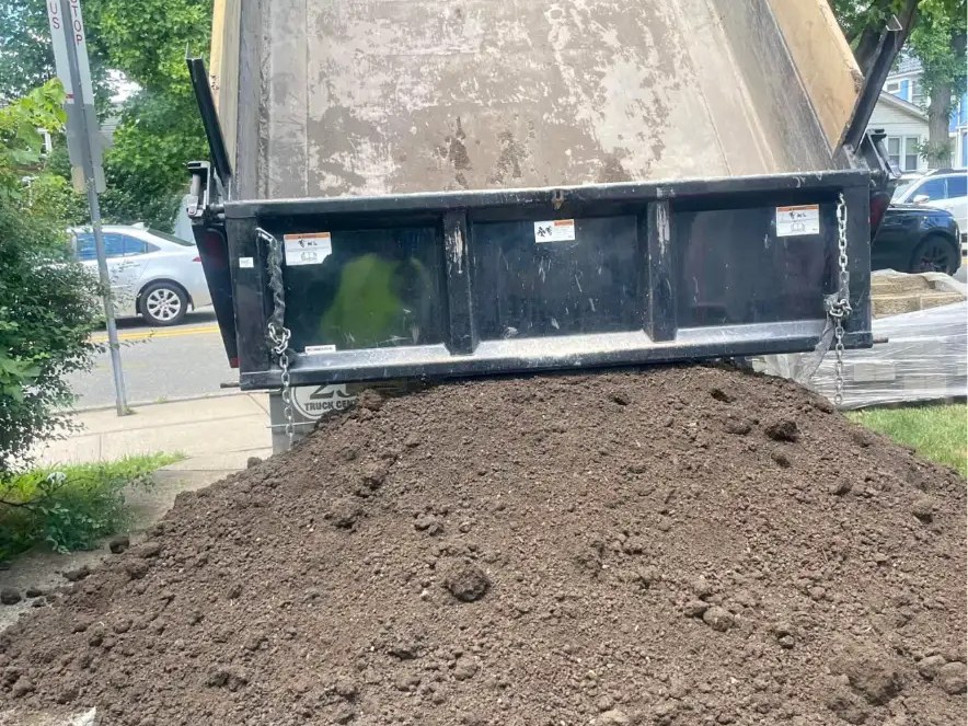 Dump truck unloading a pile of screened topsoil at a New Jersey home